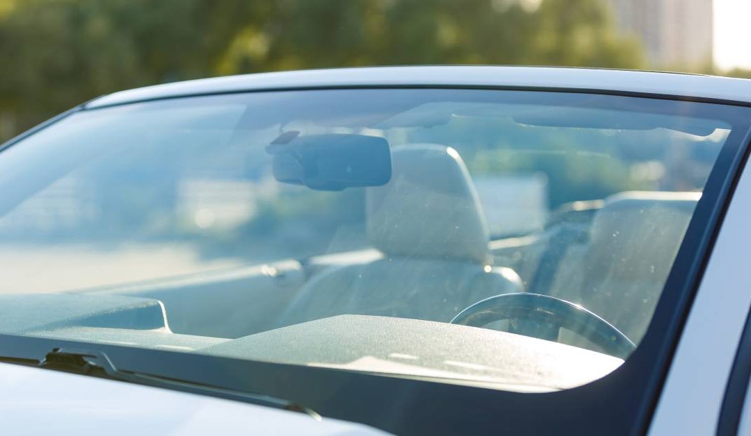 A parked car with a clean windshield and the wipers down. The seats and steering wheel are visible.