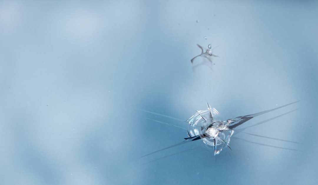 A car windshield with a star-shaped crack in it. There’s another smaller crack above it, but the two aren’t touching.