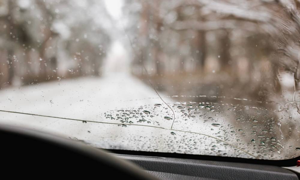 A driver’s point-of-view inside a car on a snowy road with a long splitting crack running down the windshield.