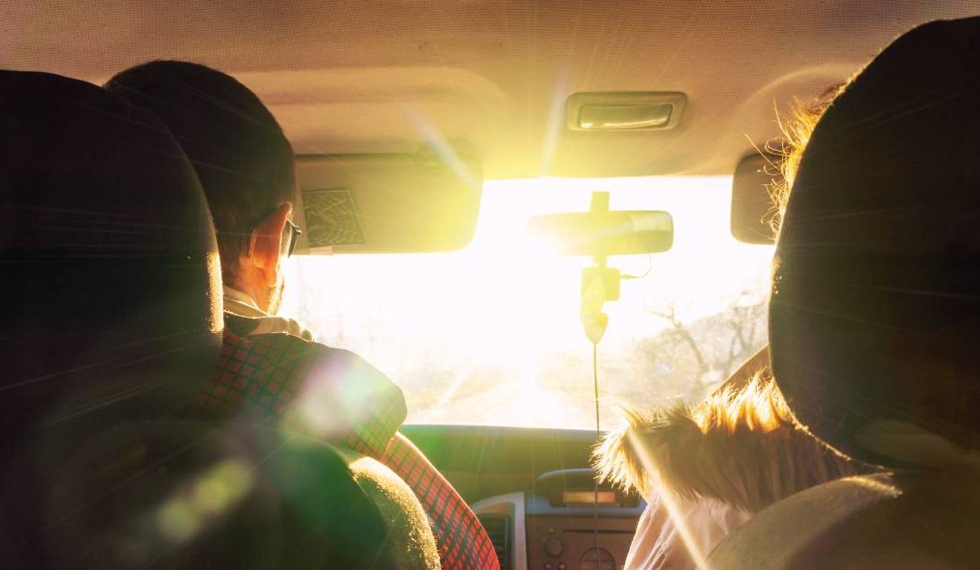 Two people sitting in the front seat of a car with their visors covering a bright glare from the sun on the windshield.