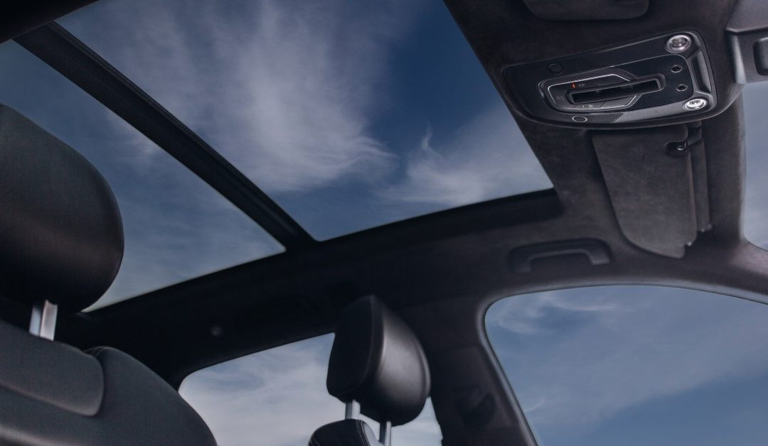 The interior of a car, with a blue sky and clouds visible through the sunroof and driver’s side window.