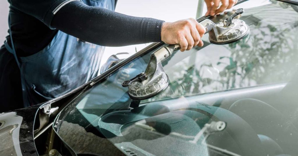 A close-up shot of a mechanic using a silver tool to install a replacement windshield on a small vehicle.