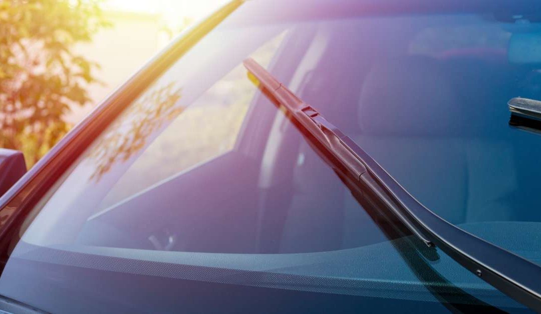 A close-up shot of a windshield on a car with the windshield wipers operating as the late-day sun shines in the background.