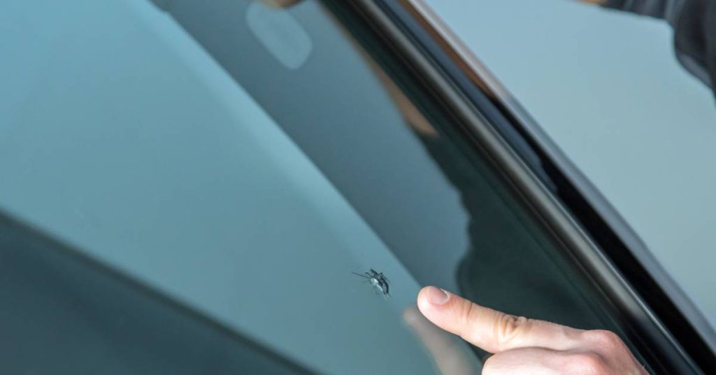 A close-up shot of a mechanic's hands as he points out a small chip on a vehicle's front windshield.