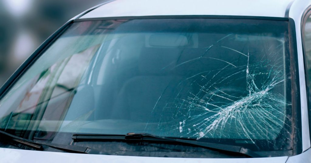 A silver vehicle has a severe crack in the windshield on the driver's side that looks to be spreading.