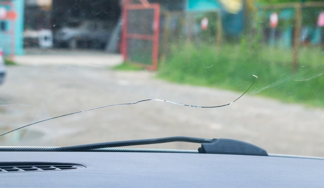 A close-up of a cracked car windshield taken from the inside of the vehicle with a building in the distance.