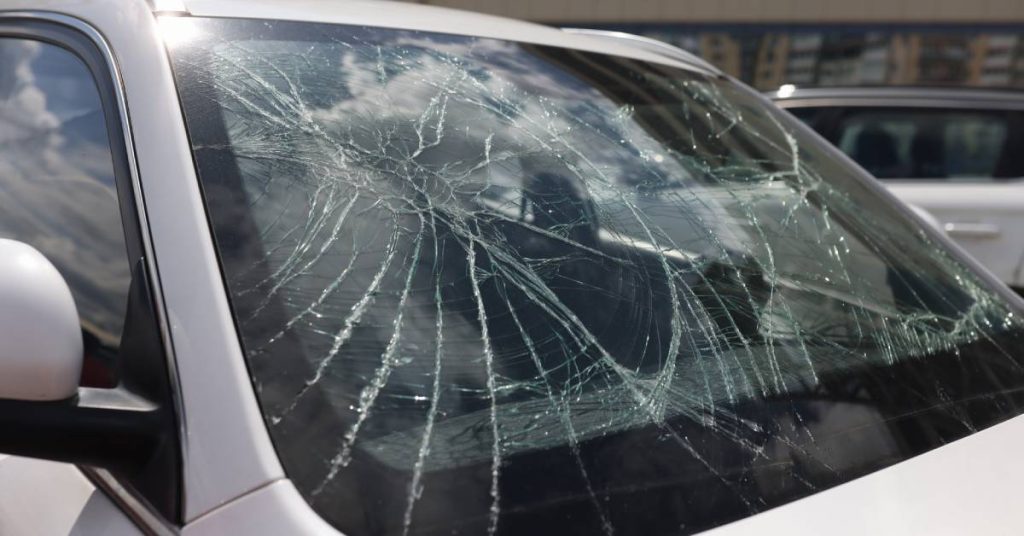 A small white vehicle with a heavily damaged windshield. The cracks create a spider's web-like design.