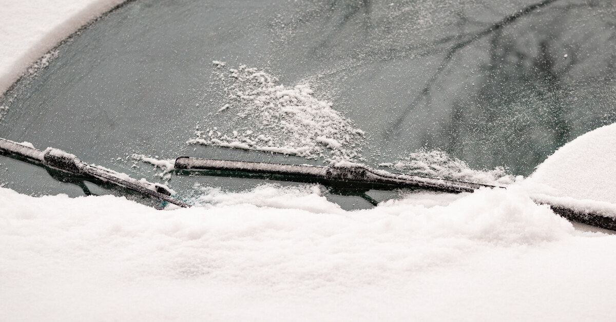 A close-up showing a small vehicle covered in a thick layer of snow being wiped away by the windshield wipers.