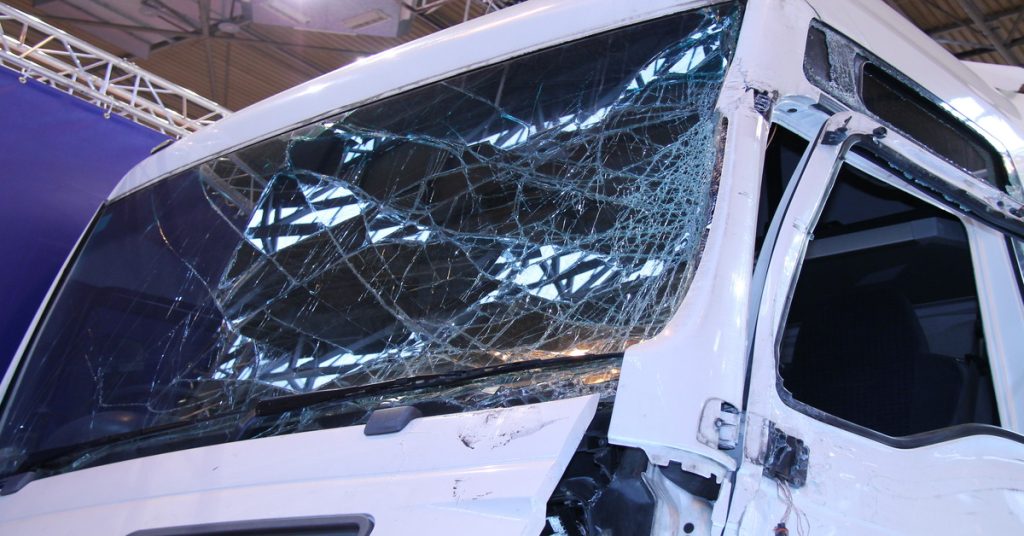 A close-up showing a large, white vehicle with an extremely damaged and cracked front windshield and window.

