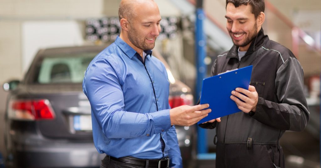 A man wearing a blue shirt and another man in a black jacket are both smiling and holding a blue clipboard.