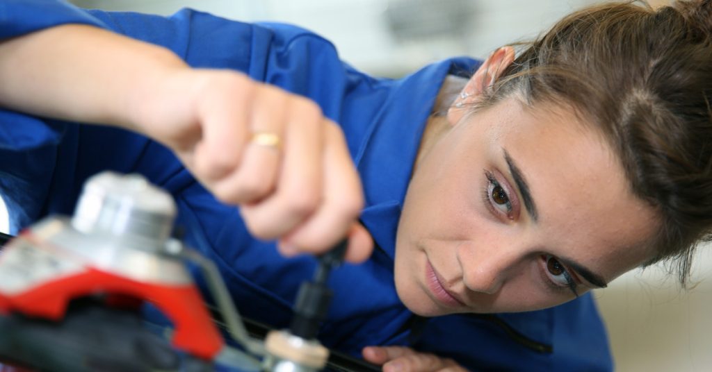 An extreme close-up showing a young woman wearing a blue shirt using a tool to repair a car's windshield.
