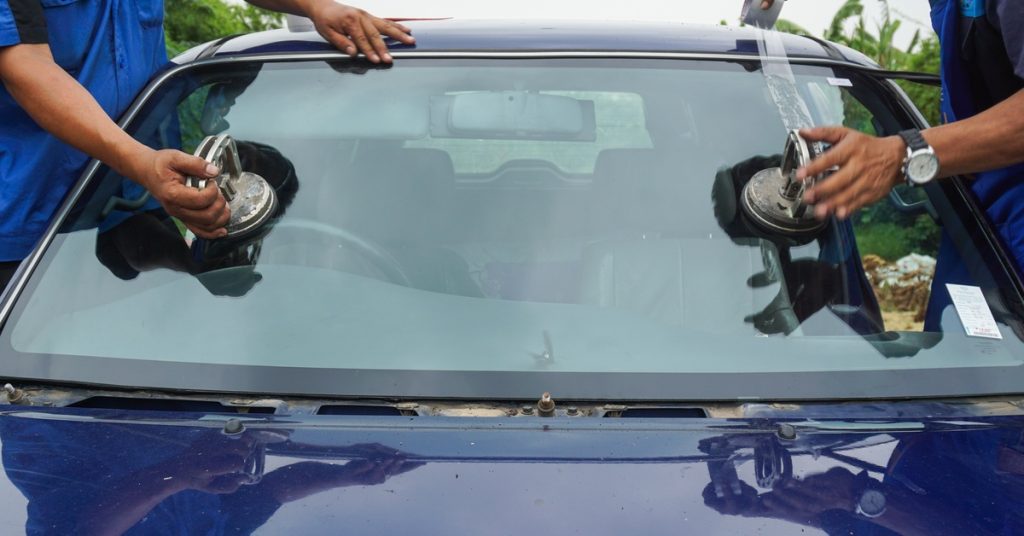 Two people wearing blue shirts are using several tools to repair the windshield of a small, blue vehicle.