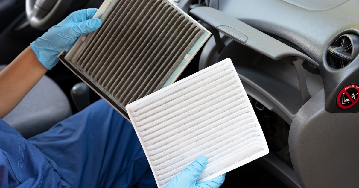 A close-up of a person wearing blue gloves holding one dirty air filter and one clean air filter inside a car.