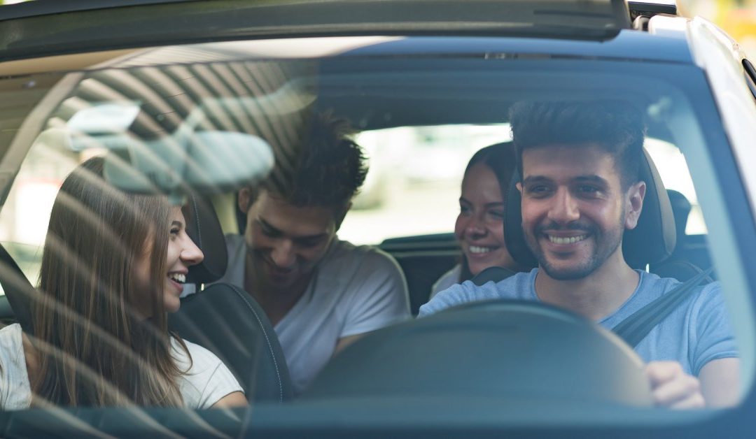 A smiling young man wearing a blue T-shirt is driving a small vehicle as the other passengers smile at each other.