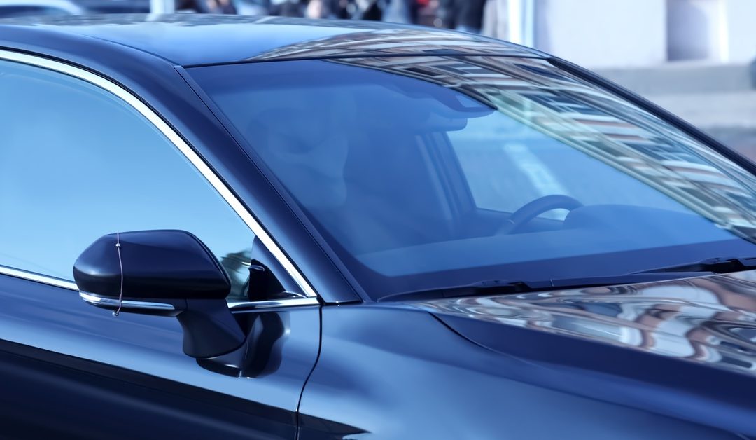 An empty, shiny, black vehicle is parked at a car dealership. The windows and windshield have a dark tint.