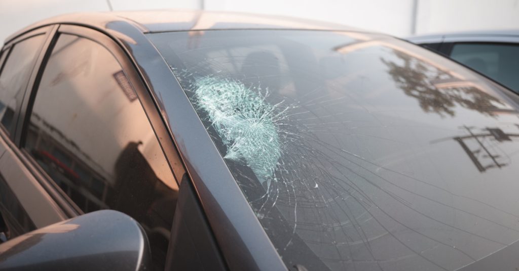 A small, black vehicle has dark, tinted windows that reflect the surroundings. The car also has a cracked windshield.
